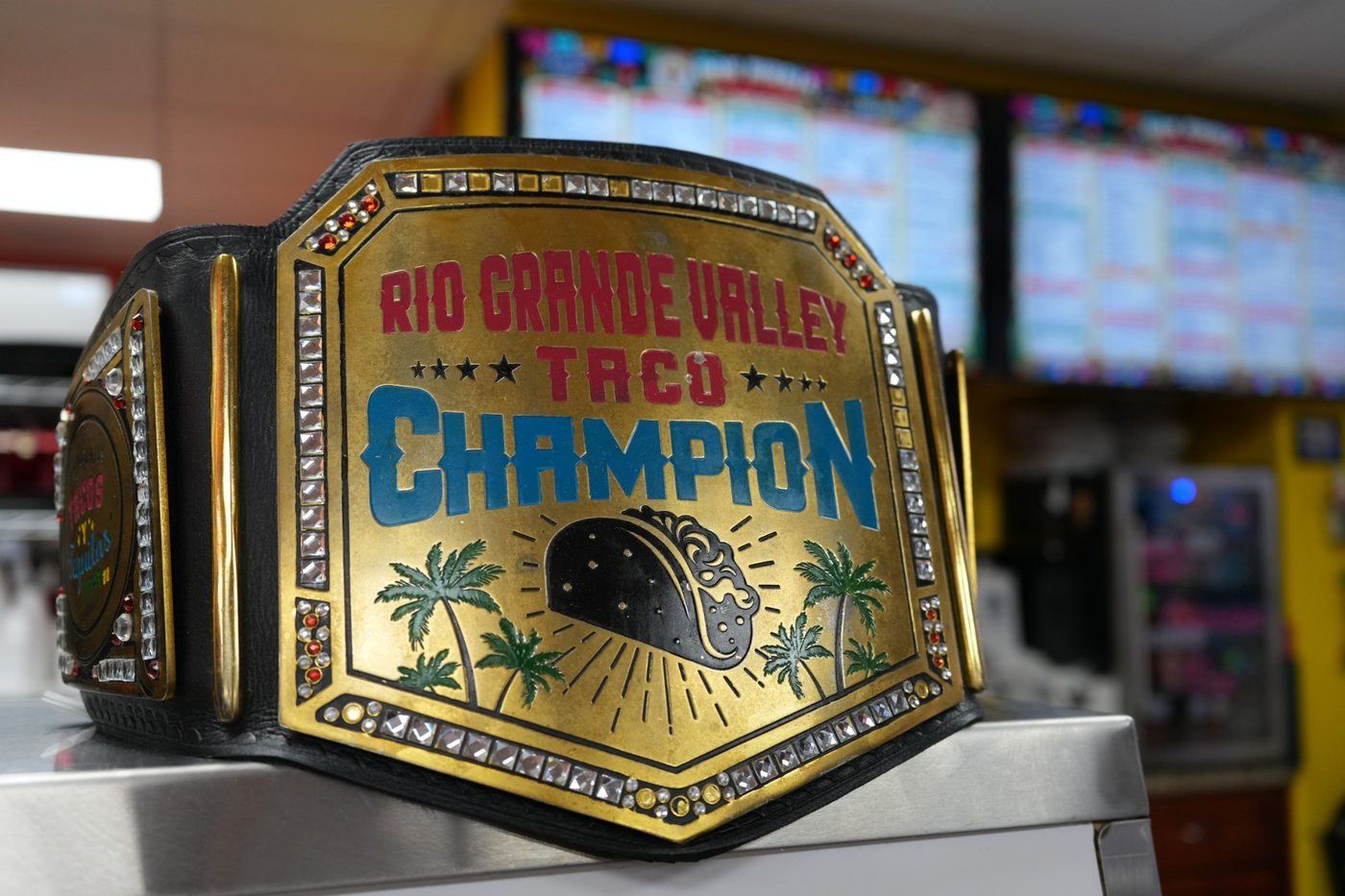 Gold championship belt reading Rio Grande Valley Taco Champion, on the counter in front of the menu boards