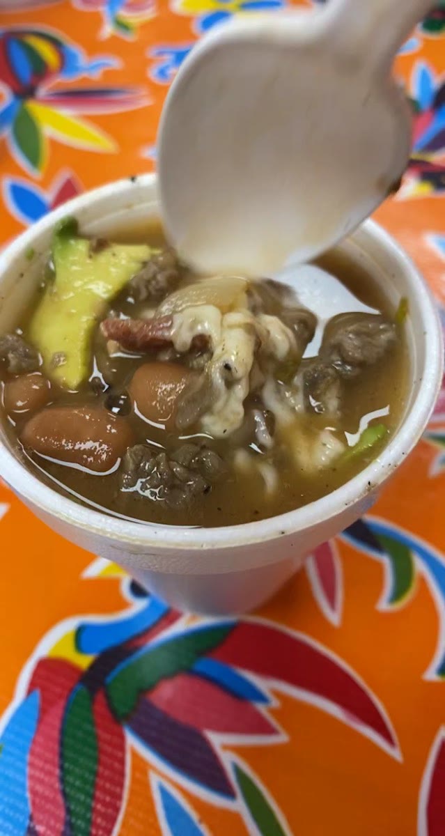 A cup of birria broth with noodles, meat and avocado